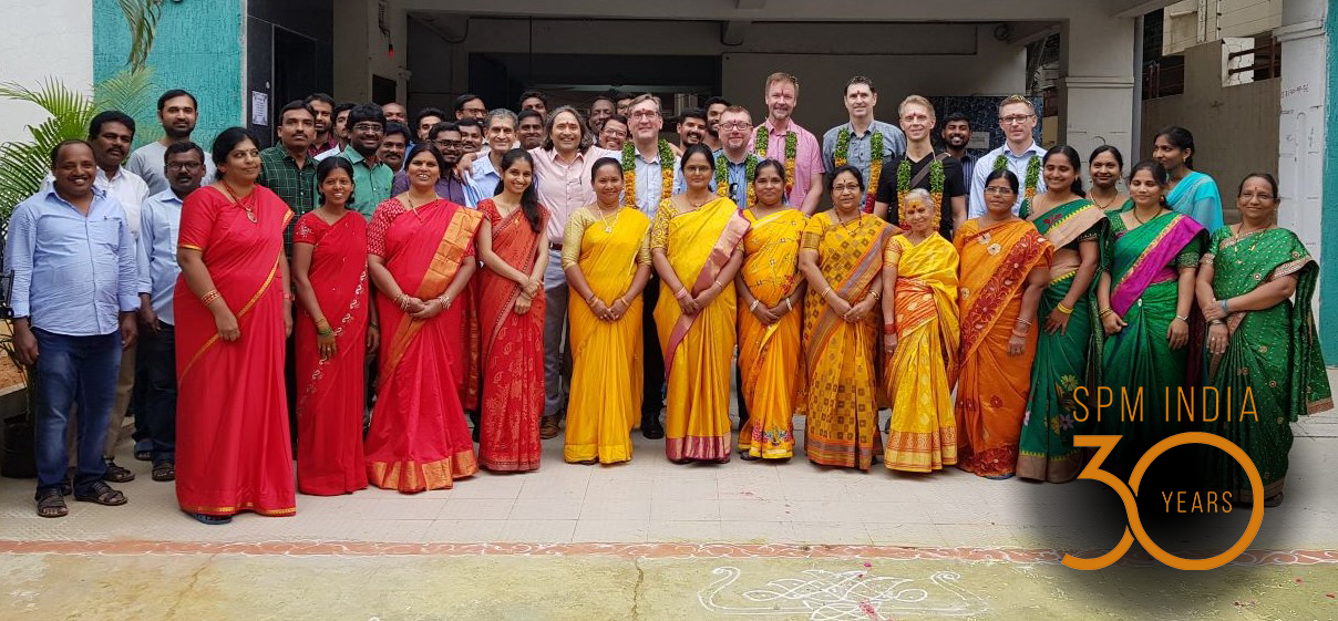 A group of people standing in front of a building with women in colorful dresses in the front row.