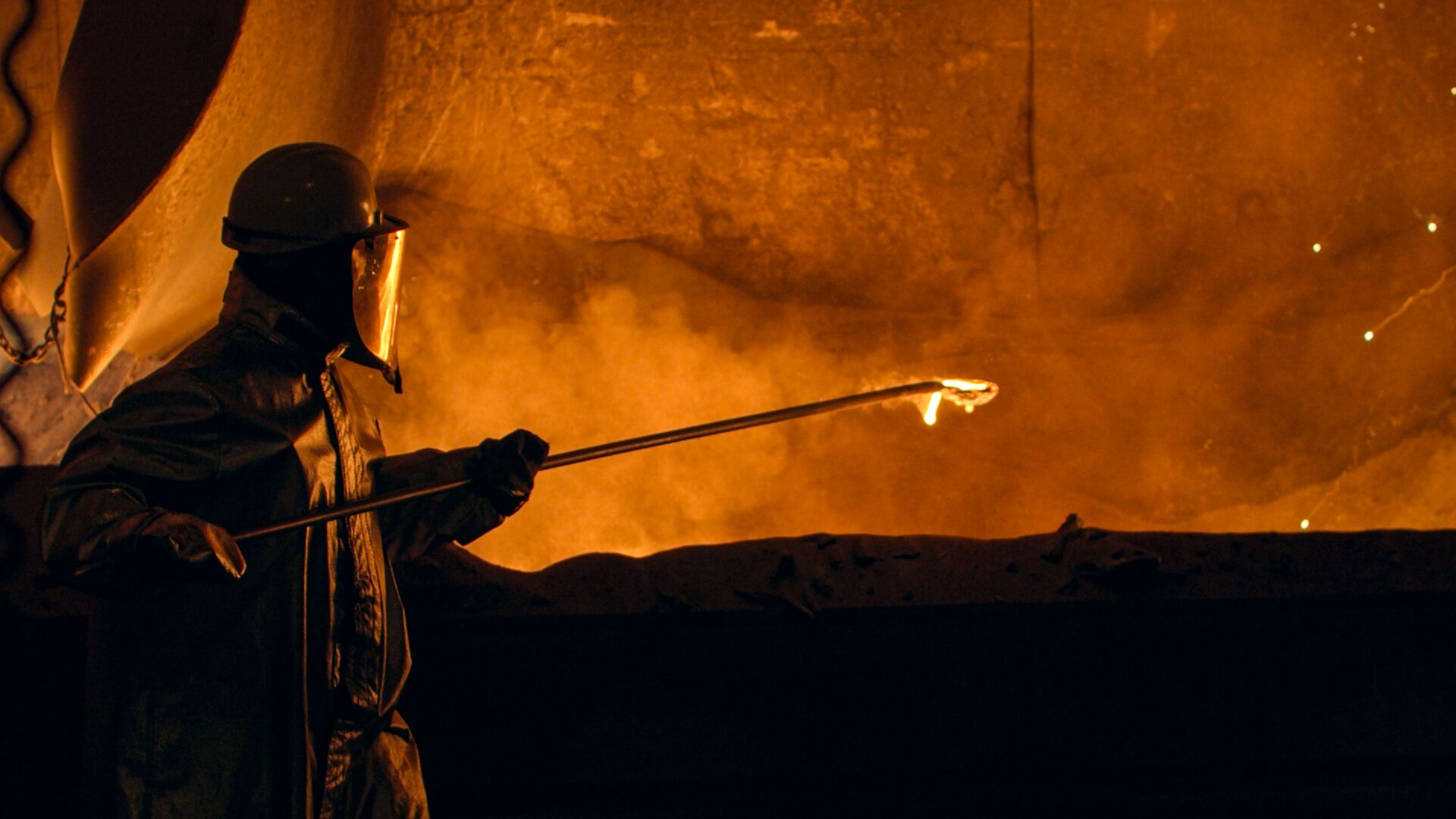 Person wearing heavy protective clothing works with casting in a smelter.