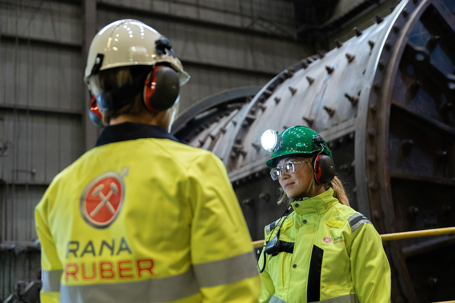 Two workers in protective clothing standing in front of an autogenous mill.